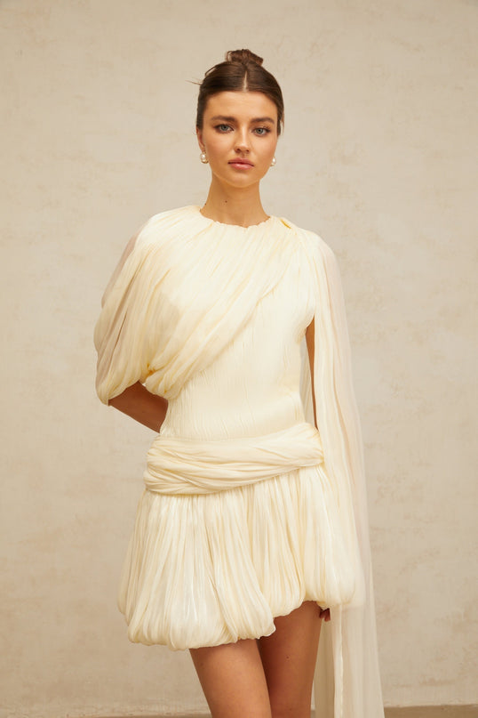 Lina Mini Dress in Neutrals Pleated Design with Ribbon Detailing and Glitter Accents Asymmetrical Silhouette Cinched Waist Bubble Hem Round Neck Twist Detailing Rear Zip Fastening Luxurious Blend of Terylene Viscose and Spandex