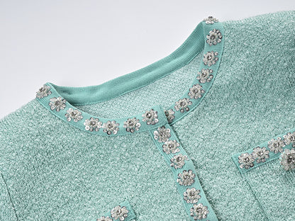 Mint green tweed jacket with floral embellishments paired with a pleated skirt, creating a chic and elegant look