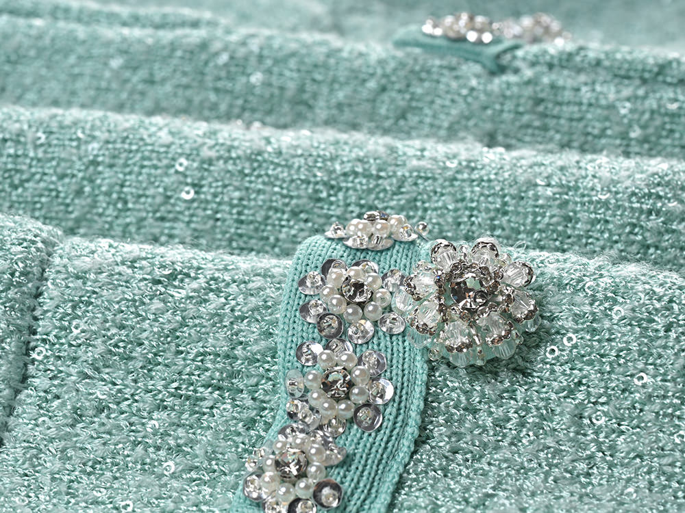 Mint green tweed jacket with floral embellishments paired with a pleated skirt, creating a chic and elegant look