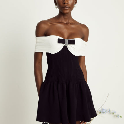 Miracle Mini Dress in Black & White off-shoulder design with crystal bow accent, thigh-length with contrasting colors and crystal embellishments, model 5'10" size M, 51% Viscose 35% Terylene 13% Nylon 2% Elastane