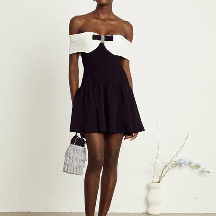 Miracle Mini Dress in Black & White off-shoulder with crystal bow accent, thigh-length with contrasting colors and crystal embellishments on model 5'10 wearing size M