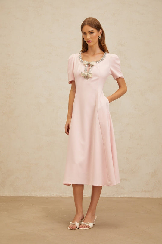 Pink short sleeve dress with crystal, faux-pearl, and bow embellishments, cinched waist, and flared hem