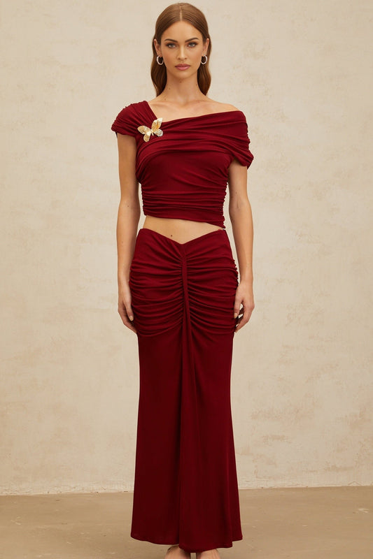 Red asymmetrical cropped top with butterfly brooch and cap sleeves, paired with red ruched mermaid hem maxi skirt