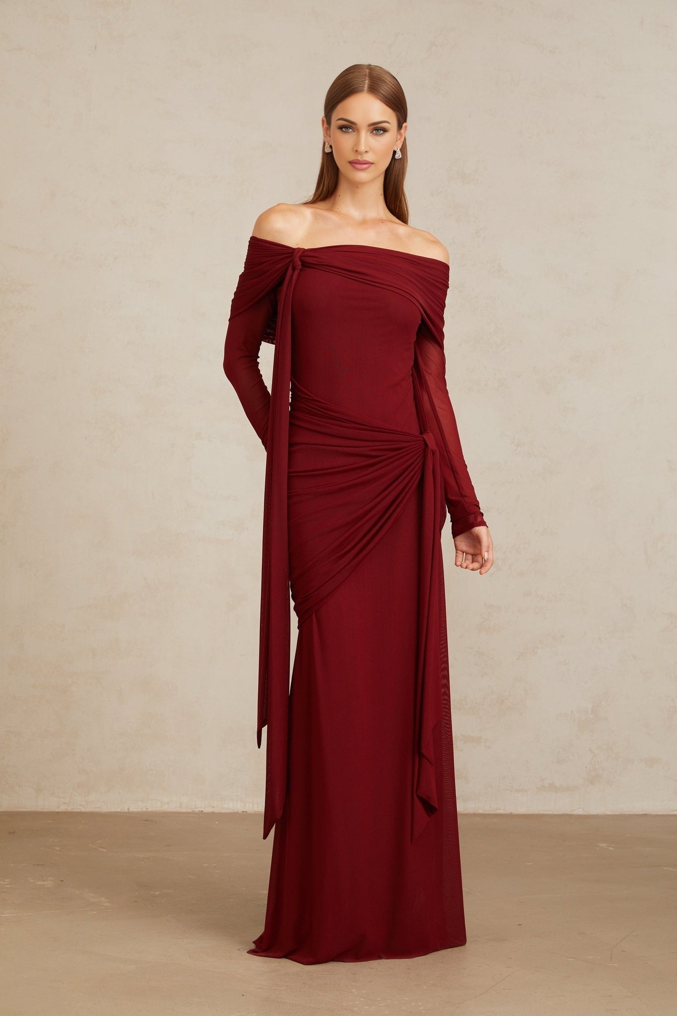 Red off the shoulder long sleeve dress with front tie detail and pleated, asymmetrical, ruched, and draped detailing, floor length