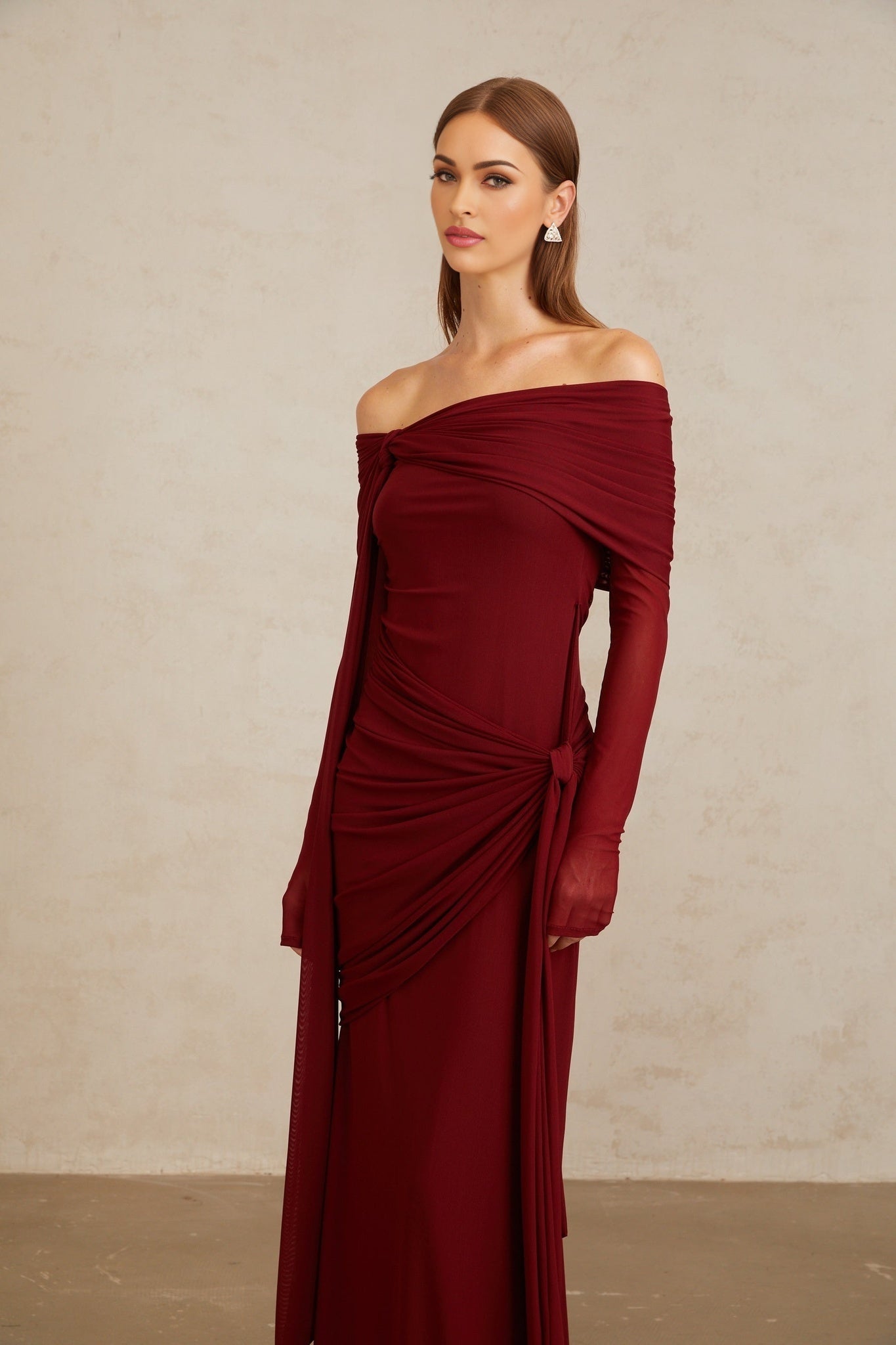 Red off the shoulder long sleeve dress with front tie detail and pleated, asymmetrical, ruched, and draped detailing, worn by model who is 1.77m tall