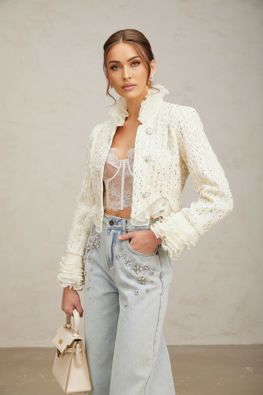 A white cropped jacket with beaded details and ruffle trim on a plain background | Hair Updated