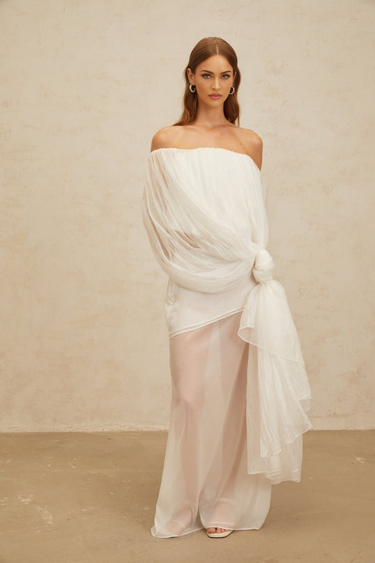 White off the shoulder tulle sleeveless top with twisted knot and asymmetrical design, paired with high rise tulle maxi skirt with draped detailing and side zip fastening