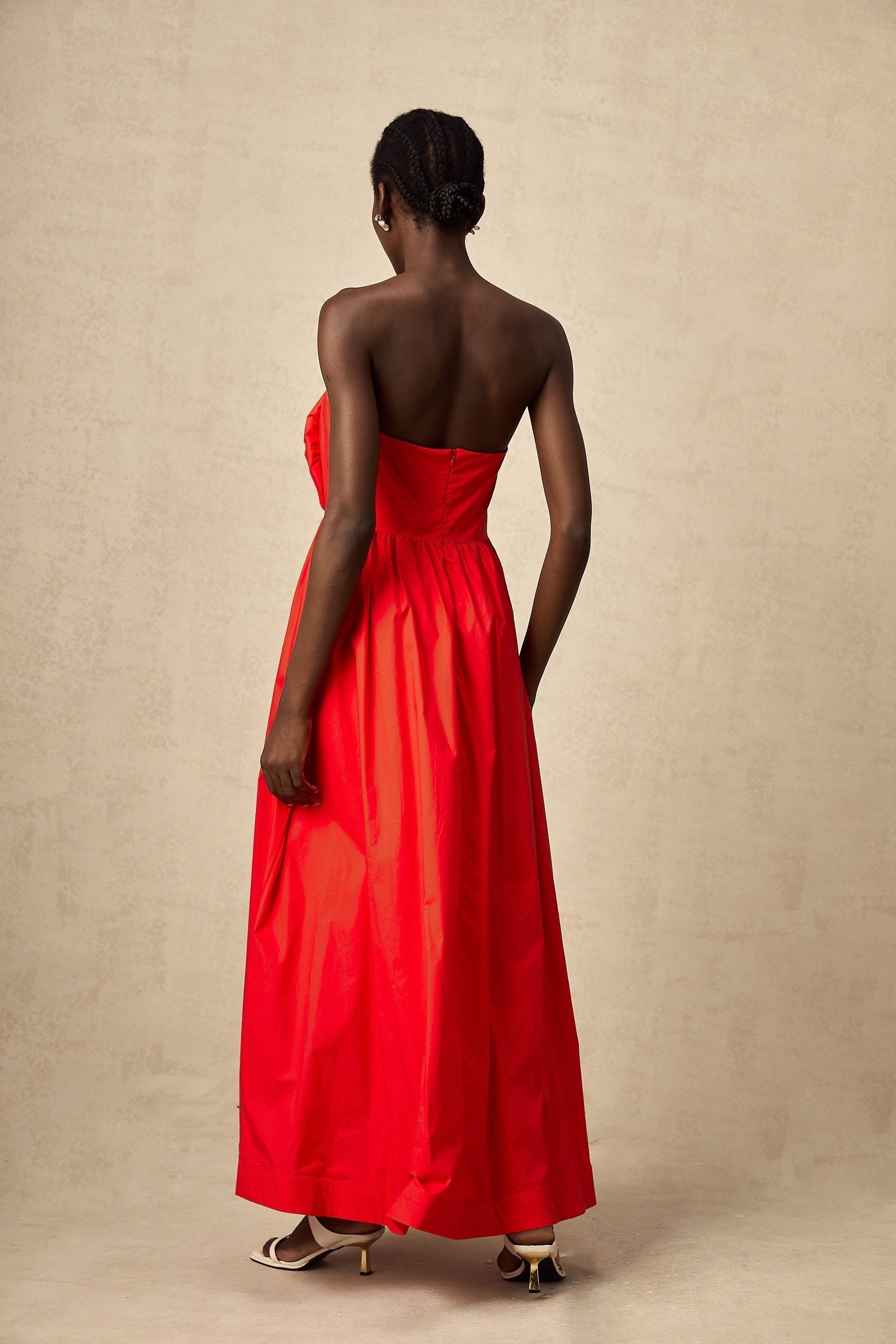 Woman in long red maxi dress with 3d ruffled petal details flowing from bodice to hem