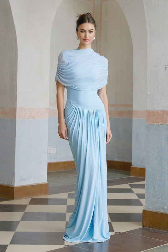 Woman wearing a baby blue asymmetric pleated maxi dress with flowing fabric and uneven hemline