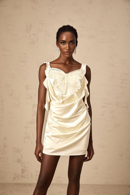 Woman wearing a beige mini dress with butterfly print and draped design standing against neutral background