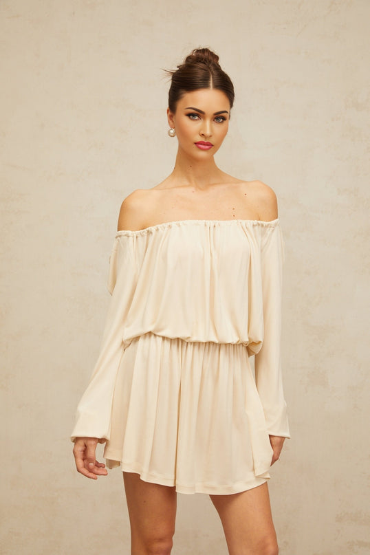 Woman wearing a beige mini dress with structured design and neutral tones standing against plain background