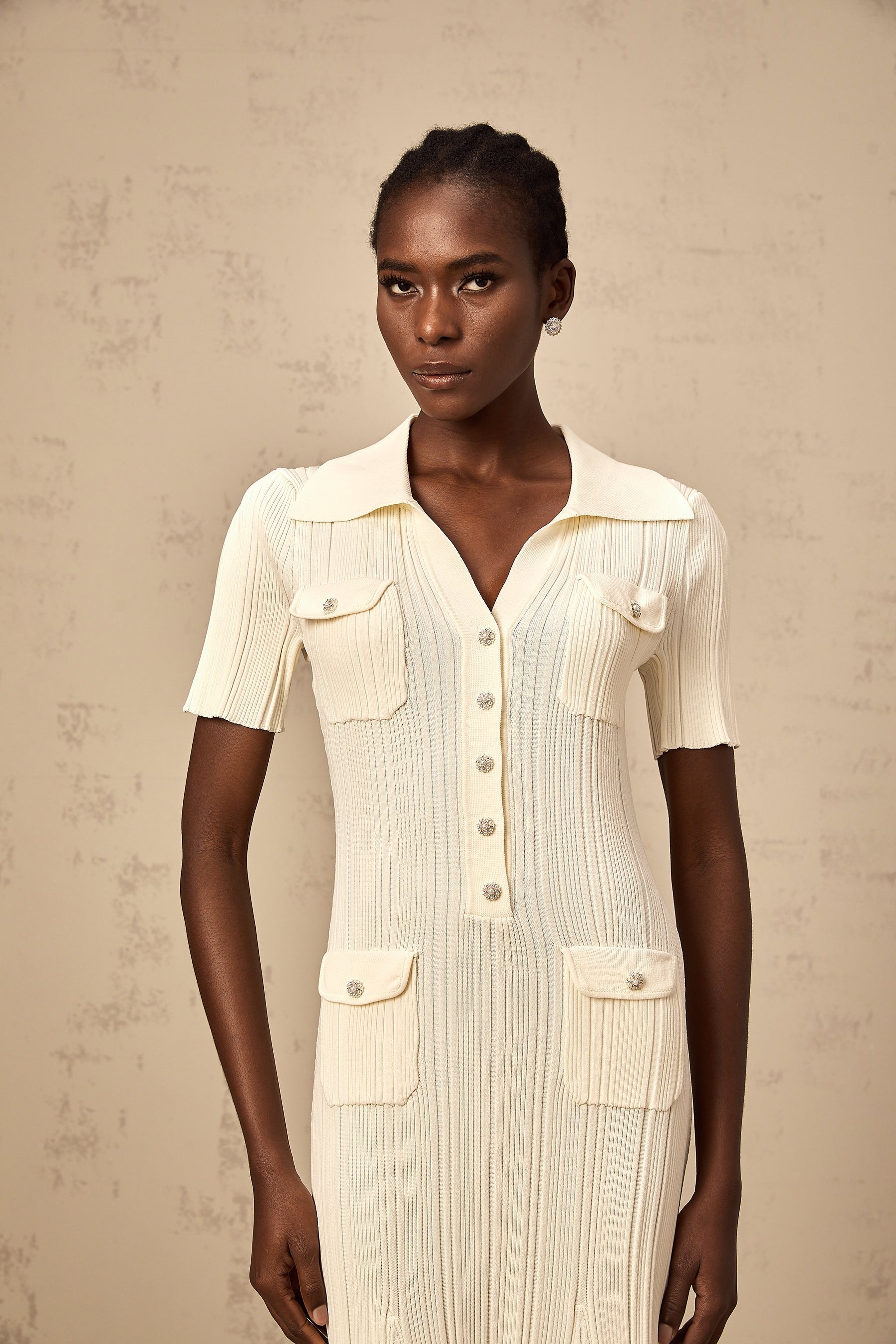 Woman wearing a beige ribbedknit midi dress with long sleeves and a fitted silhouette standing against a neutral background