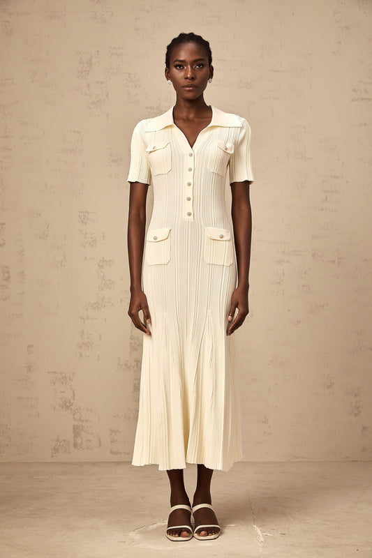 Woman wearing a beige ribbedknit midi dress with long sleeves and a formfitting silhouette standing against a plain background