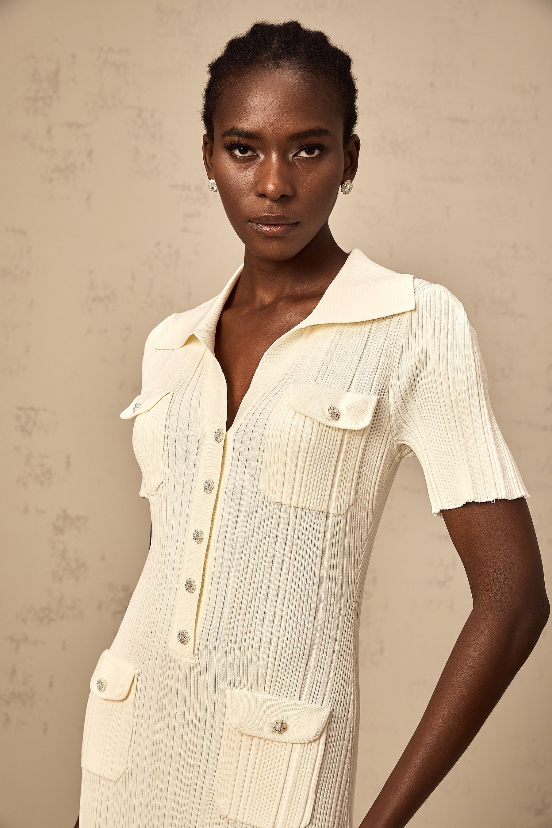 Woman wearing a beige ribbedknit midi dress with long sleeves and a formfitting silhouette standing against a plain background
