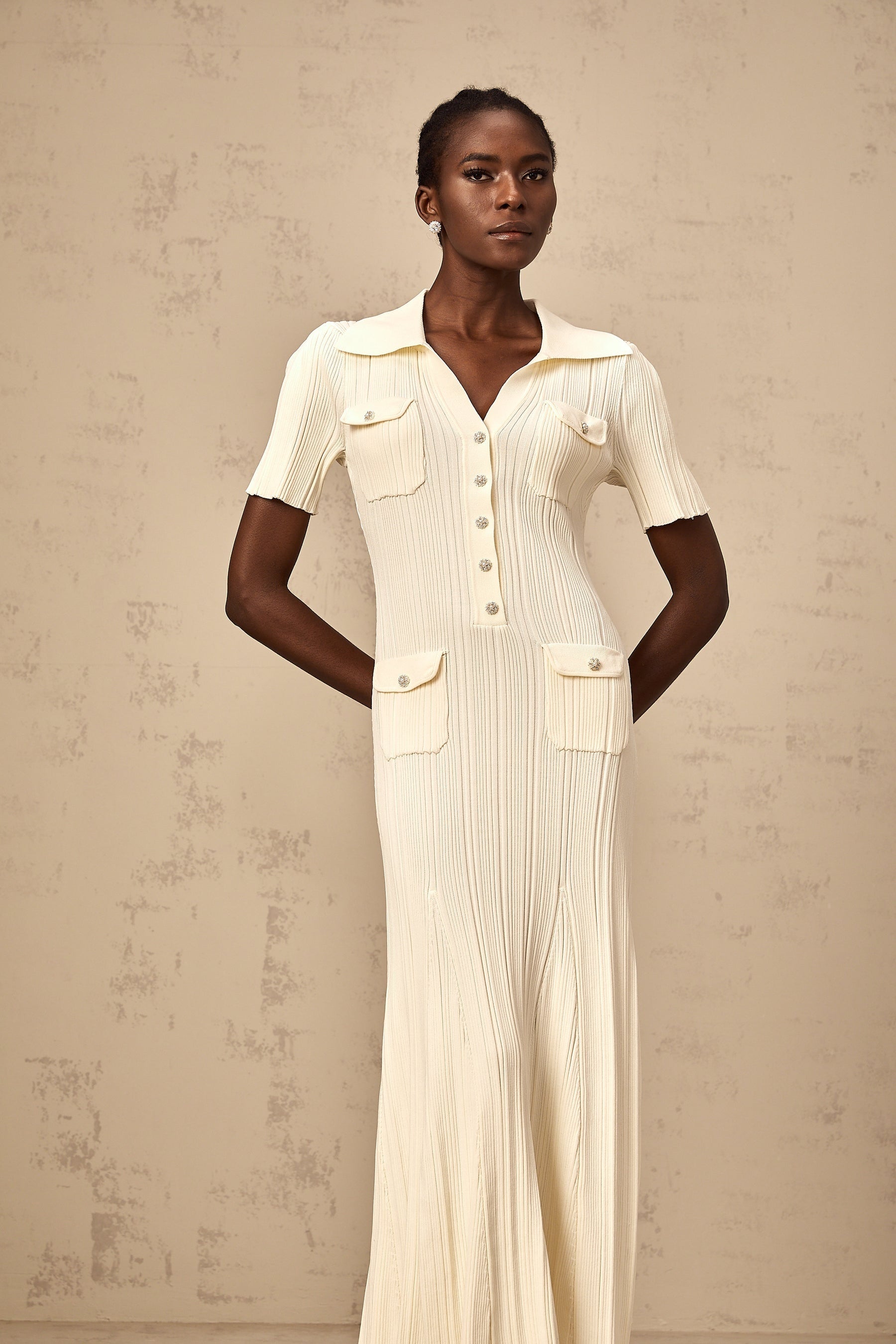 Woman wearing a beige ribbedknit midi dress with long sleeves and a formfitting silhouette standing against a plain background