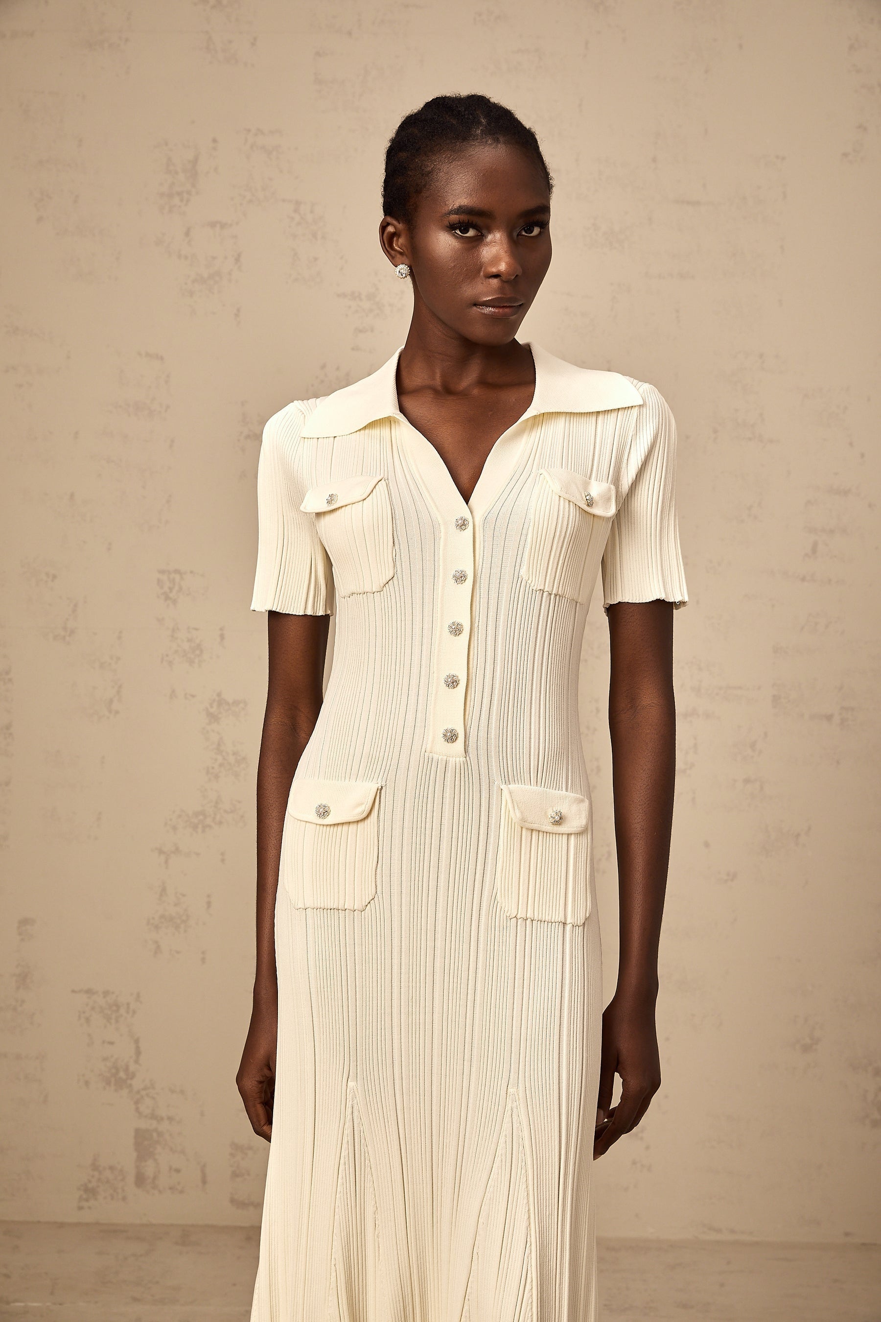 Woman wearing a beige ribbedknit midi dress with long sleeves and a formfitting silhouette standing in a neutral background