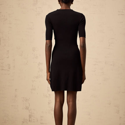 Woman wearing a black fine knit mini dress with decorative buttons standing in a neutral pose against a plain background