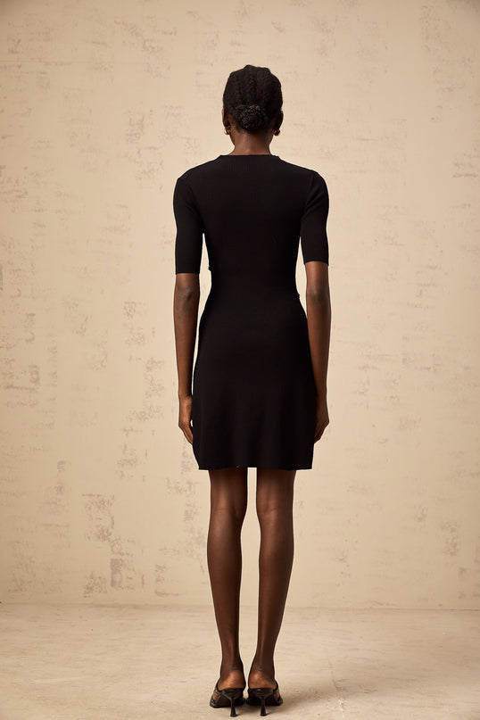 Woman wearing a black fine knit mini dress with decorative buttons standing in a neutral pose against a plain background