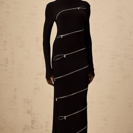 Woman wearing a black fitted maxi dress with zipper details standing against a plain background