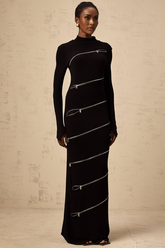 Woman wearing a black fitted maxi dress with zipper details standing against a plain background