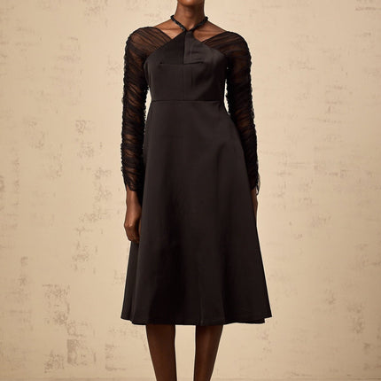 Woman wearing a black halterneck midi dress with panel detailing form fitting silhouette and sleek design