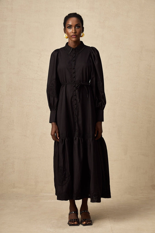 Woman wearing a black lace midi dress with embroidered details standing against a plain background