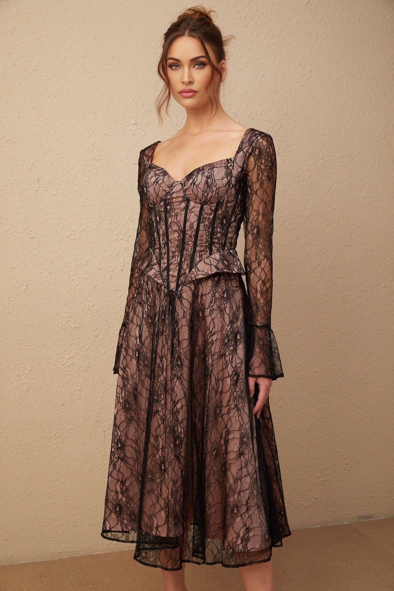 Woman wearing a black lace midi dress with flared skirt and fitted bodice standing against plain background