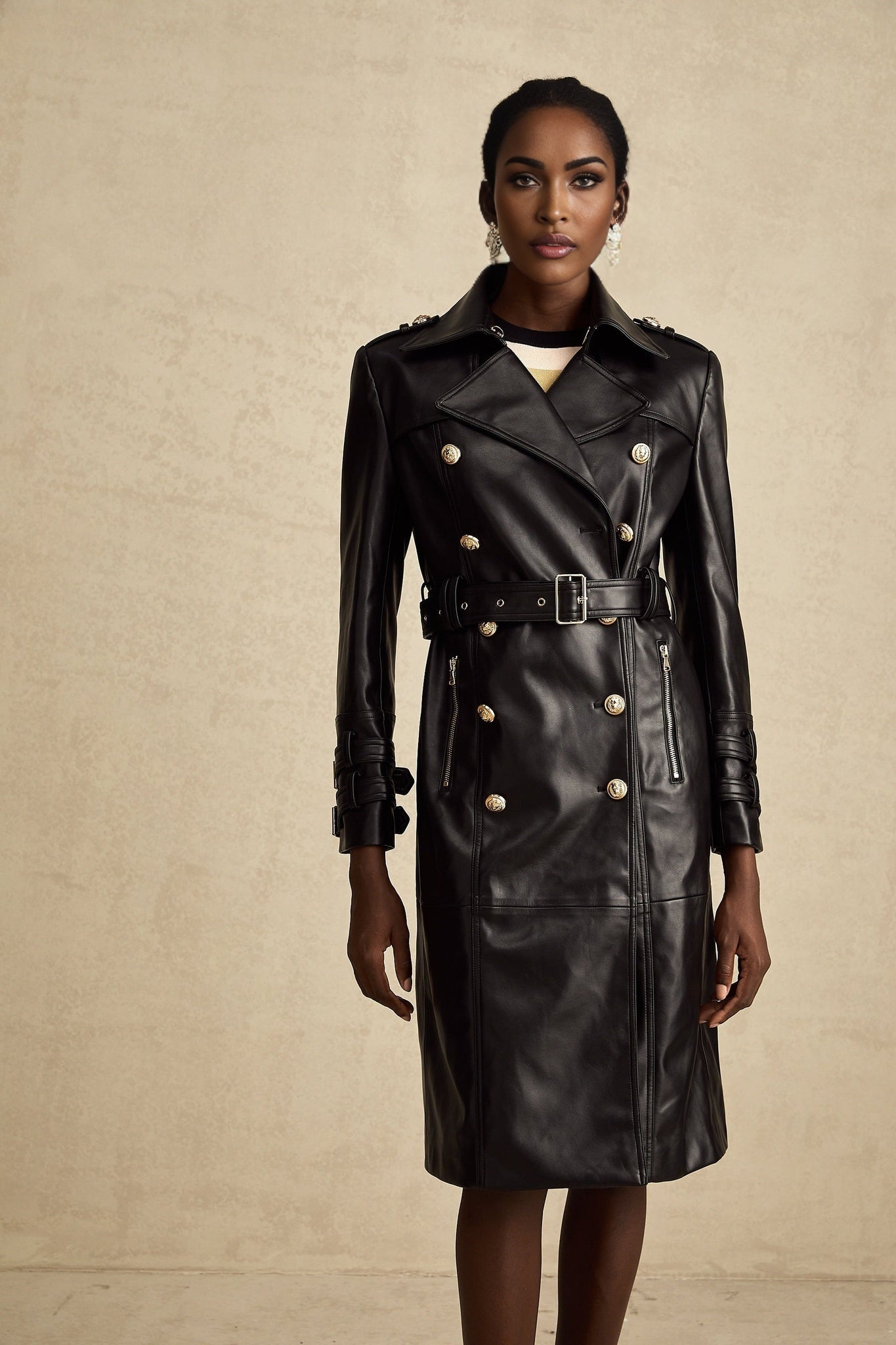 Woman wearing a black leather coat with double breasted front and belt cinched at waist