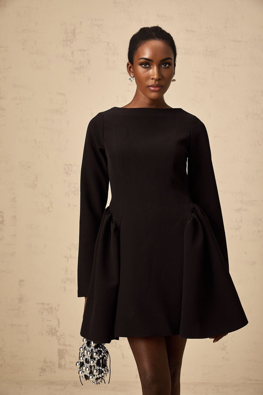 Woman wearing a black long sleeve mini dress with flared skirt standing against plain background