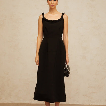 Woman wearing a black midi dress with braided details and puff sleeves standing against a plain background