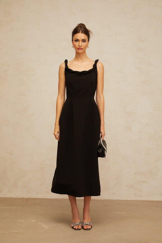 Woman wearing a black midi dress with braided details and puff sleeves standing against a plain background