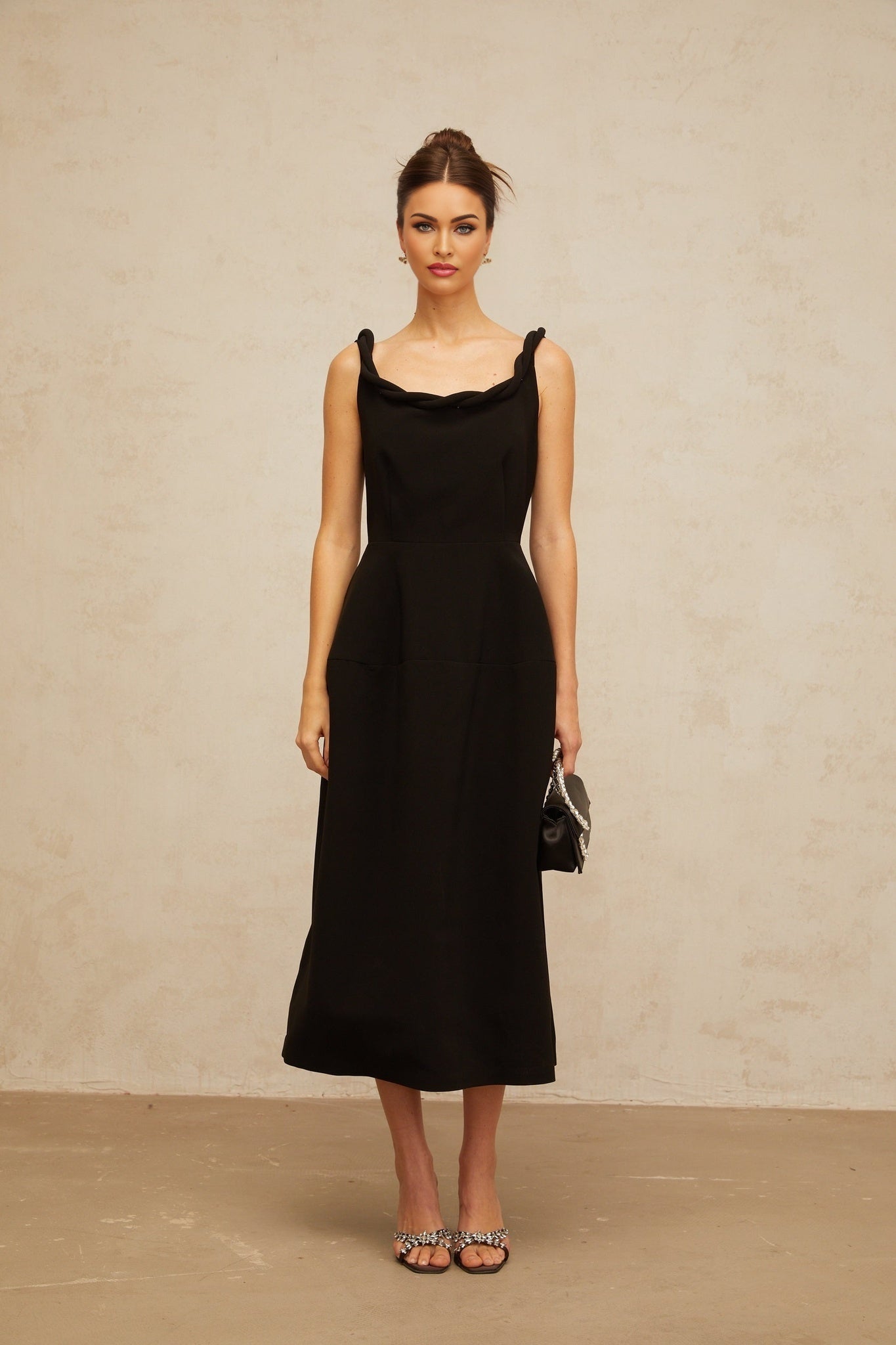 Woman wearing a black midi dress with braided details and puff sleeves standing against a plain background