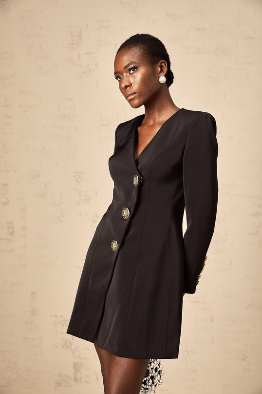 Woman wearing a black mini dress with a blazer style top featuring decorative lion head details on the shoulders