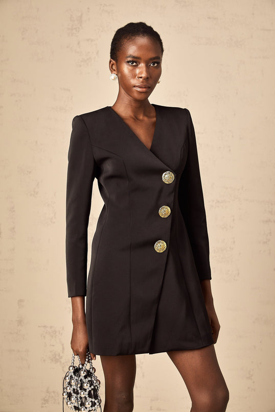 Woman wearing a black mini dress with lion head embellishments on the blazer style top form fitting silhouette short skirt length