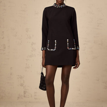 Woman wearing a black mini dress with long sleeves and crystal embellishments