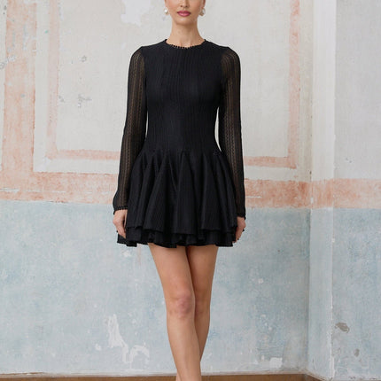 Woman wearing a black mini dress with puff sleeves and pointelle detailing standing against a plain background