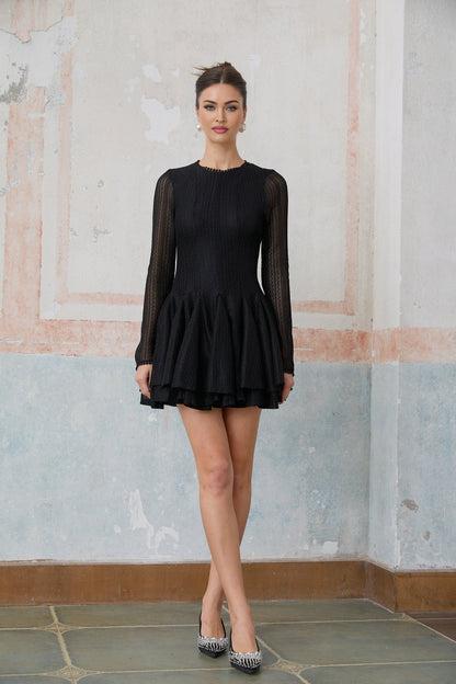 Woman wearing a black mini dress with puff sleeves and pointelle detailing standing against a plain background