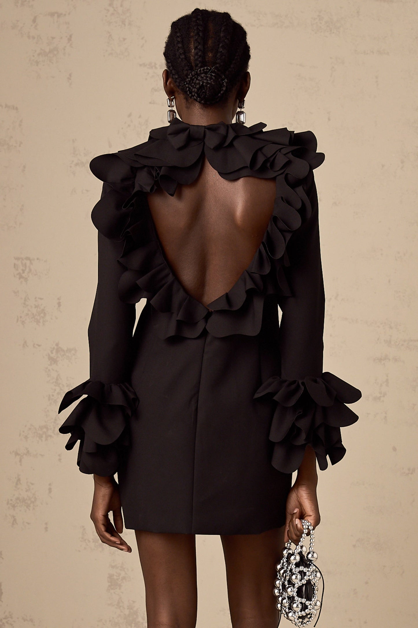 Woman wearing a black mini dress with ruffled details and an open back design
