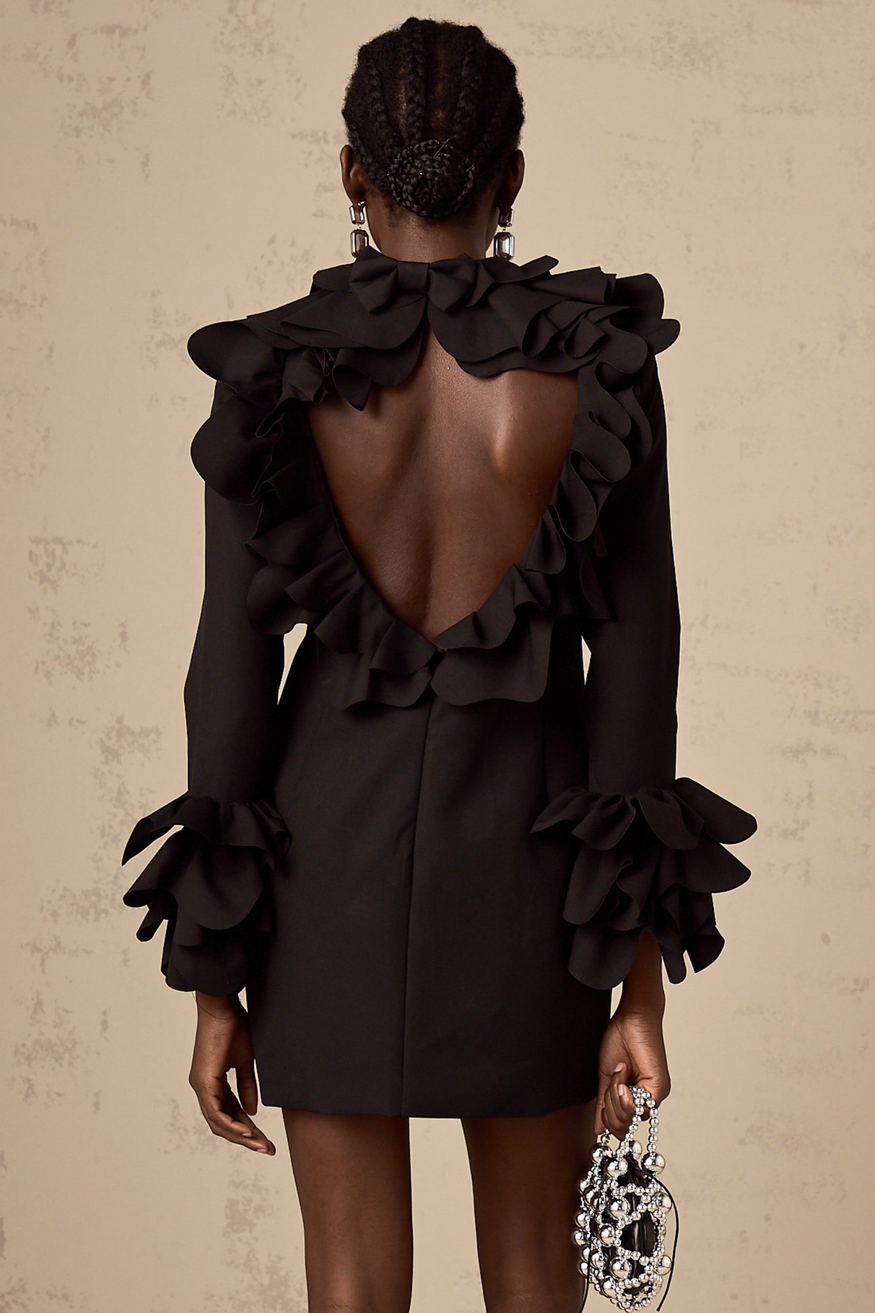 Woman wearing a black mini dress with ruffled details and an open back design