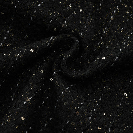 Woman wearing a black mini dress with tweed fabric and sequin panels standing in a neutral background