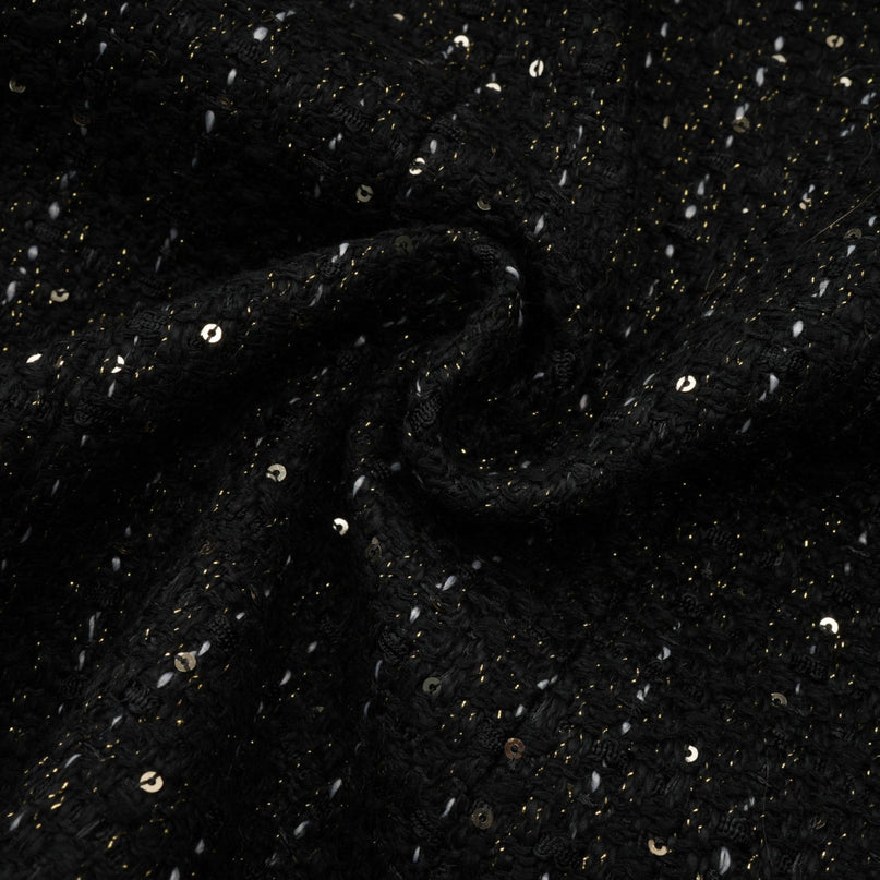 Woman wearing a black mini dress with tweed fabric and sequin panels standing in a neutral background