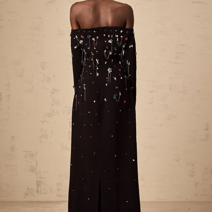 Woman wearing a black offshoulder maxi dress with crystal embellishments standing in an elegant pose