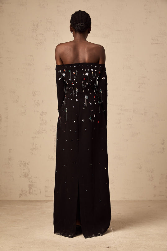 Woman wearing a black offshoulder maxi dress with crystal embellishments standing in an elegant pose