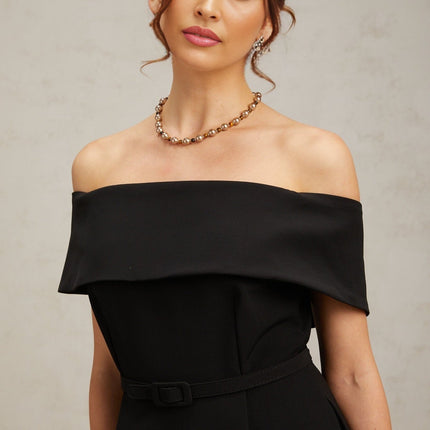 Woman wearing a black offshoulder mini dress with a belt cinched at the waist standing against a plain background