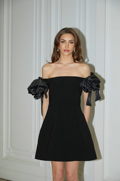 Woman wearing a black offshoulder mini dress with flower details on the bodice