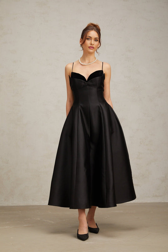 Woman wearing a black pleated midi dress with flared skirt and long sleeves standing in a neutral pose