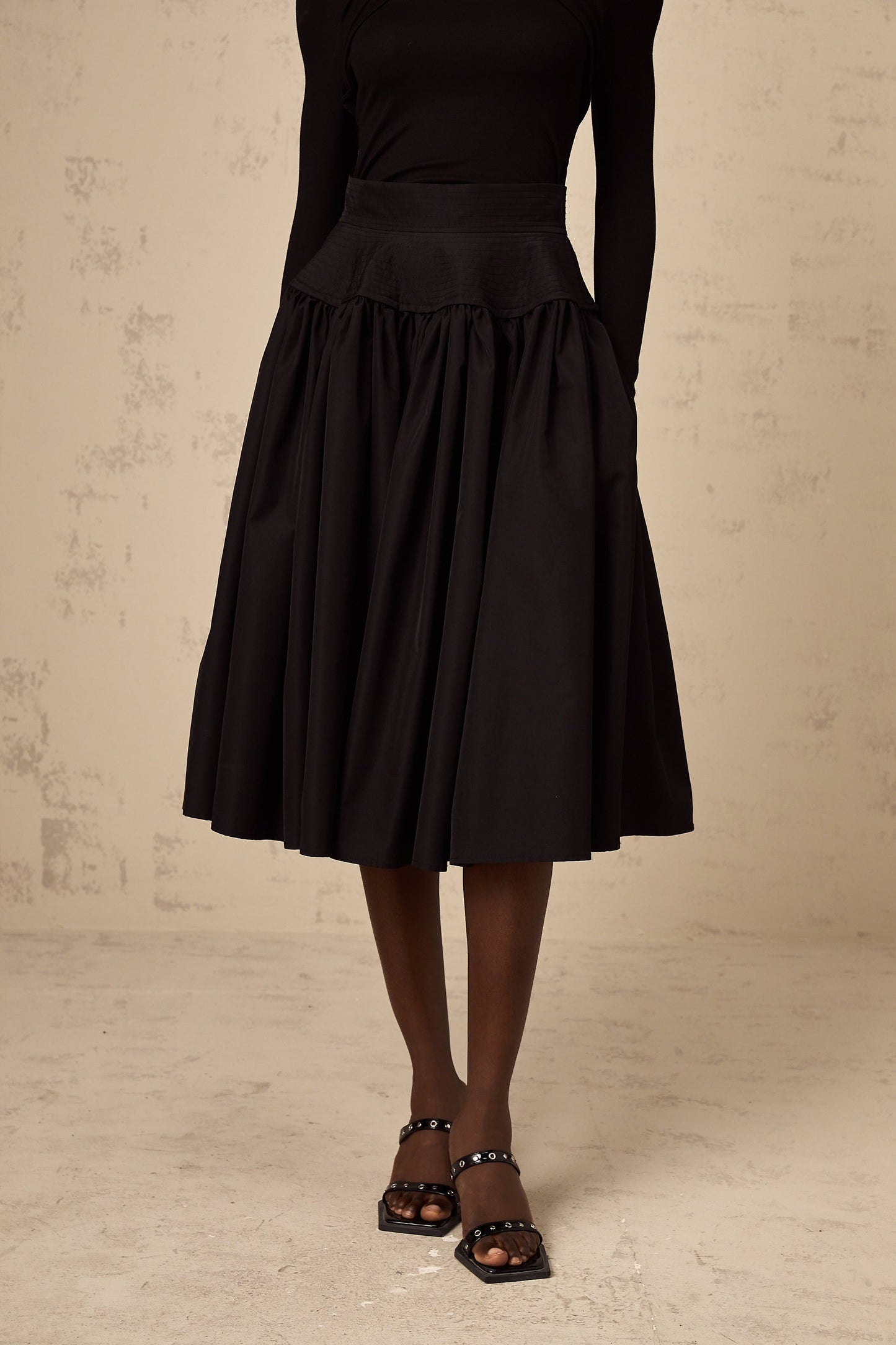 Woman wearing a black pleated midi skirt with a flared silhouette