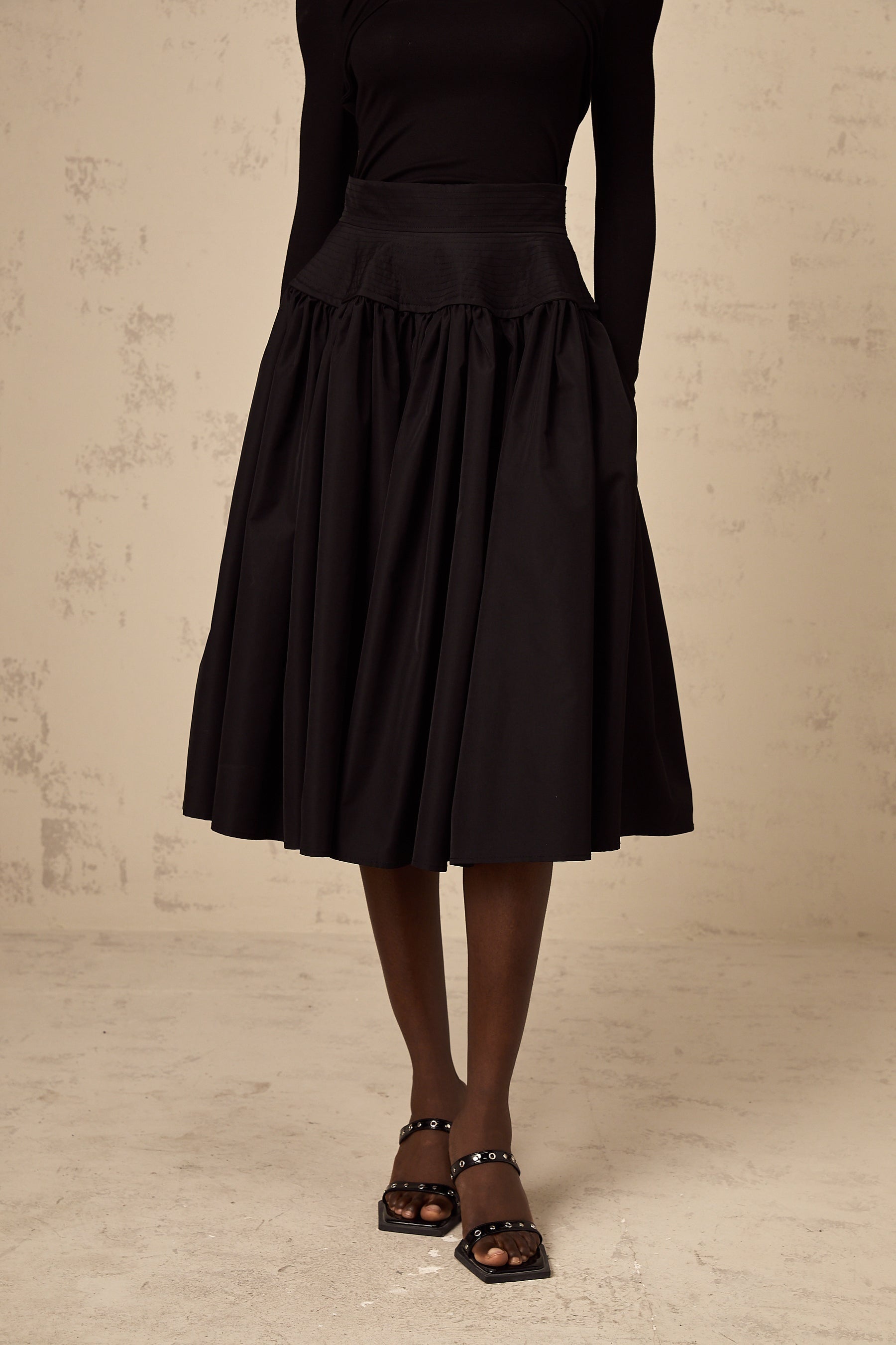 Woman wearing a black pleated midi skirt with a flared silhouette