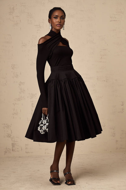Woman wearing a black pleated midi skirt with flared silhouette standing against a plain background