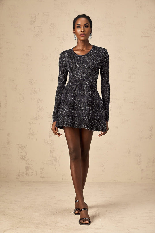 Woman wearing a black sequined knit mini dress with short sleeves and a form fitting silhouette
